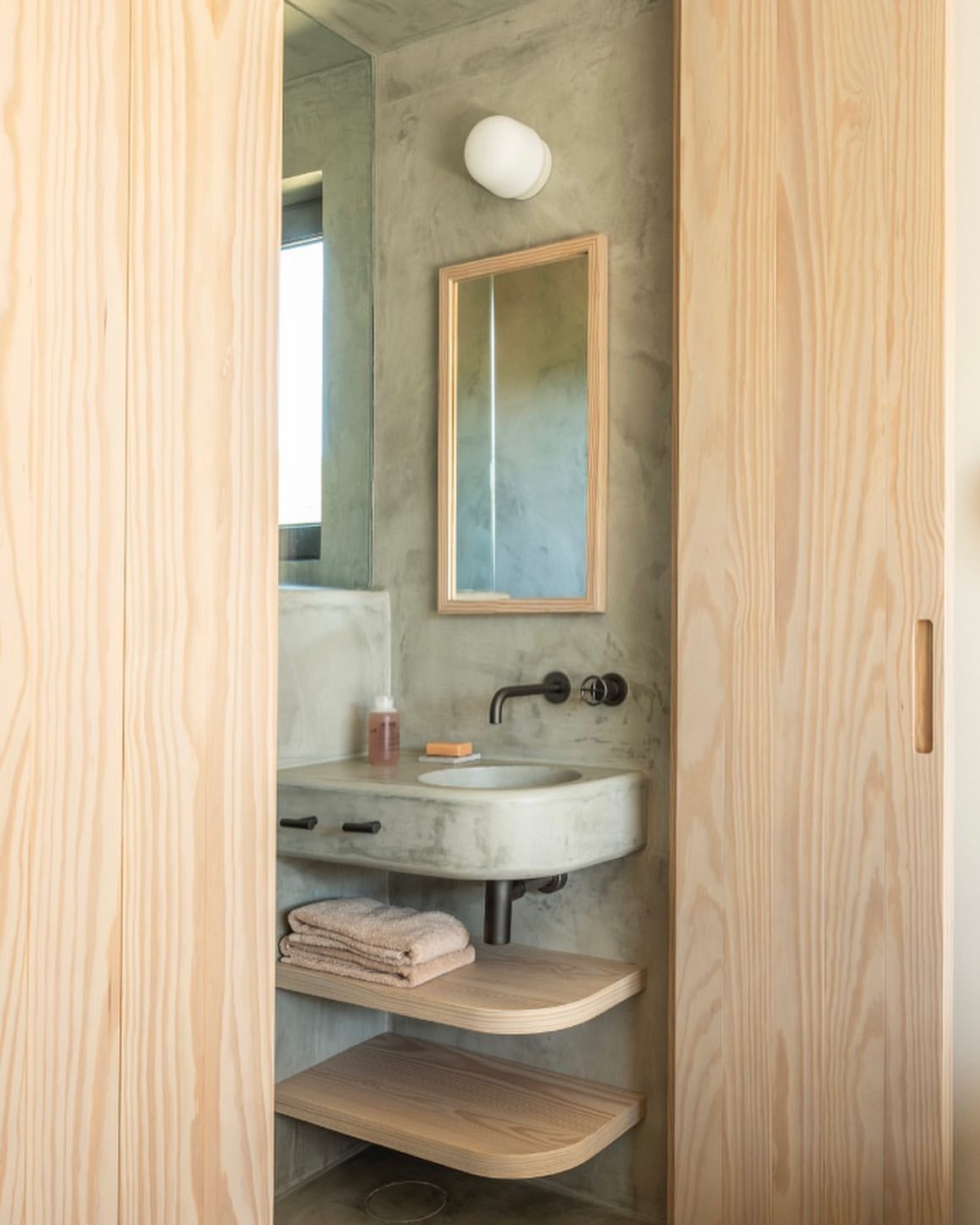 Modern bathroom interior featuring a concrete sink, wooden cabinets, a framed mirror, and neutral color scheme, creating a minimalist aesthetic.
