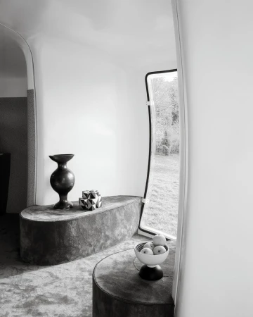 Modern interior space featuring a table with decorative vase, geometric figure, bowl of apples near a window, in monochrome.