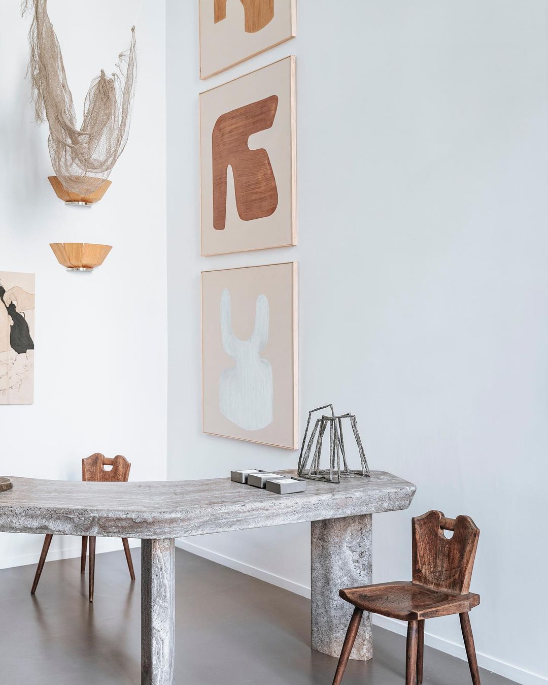 Minimalist interior featuring a light stone table, wooden chairs, and framed abstract art in a bright, modern space.