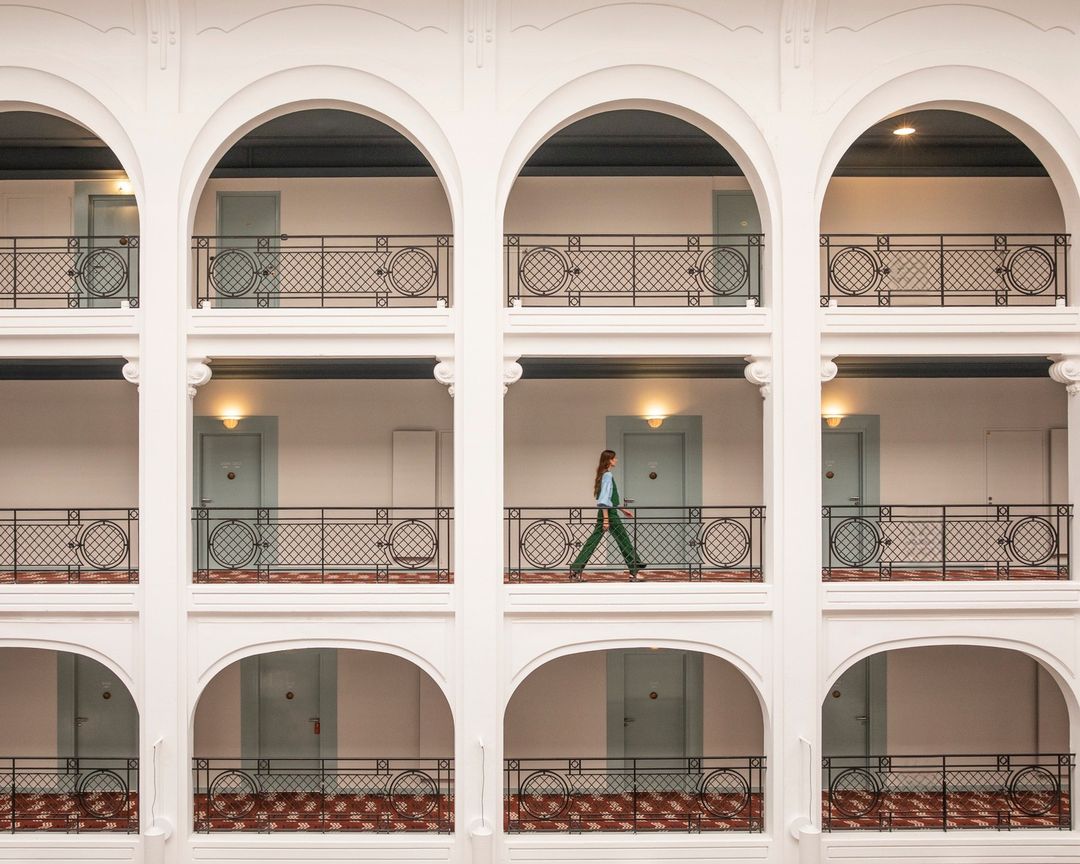 Woman walking along hotel balcony with archways in a high angle architectural shot on a sunny day indoors.