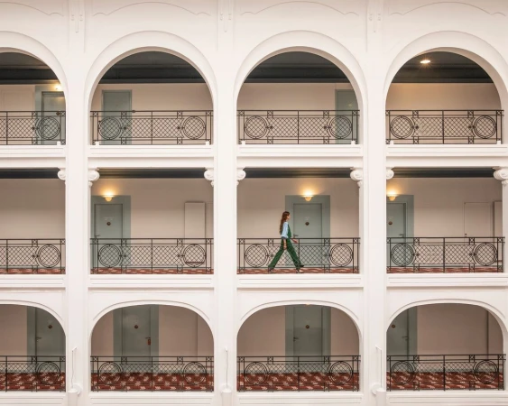 Woman walking along hotel balcony with archways in a high angle architectural shot on a sunny day indoors.