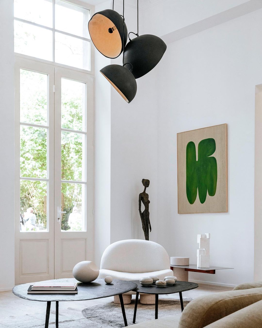 Living room interior with a modern black pendant light fixture, artwork, white chair, and layered coffee tables in a well-lit space.