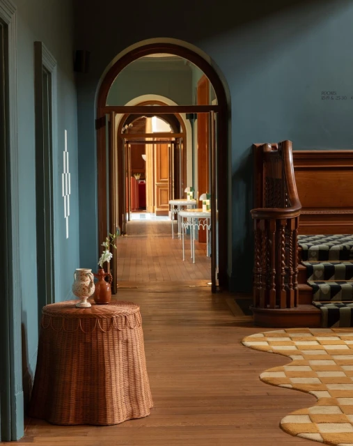 Interior of a hallway with a table in the foreground, archways leading to other rooms, a staircase, and blue-painted walls.