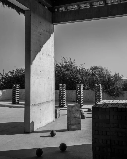 Monochrome image of an outdoor architectural space with concrete structures, spherical objects, and curated greenery against a bright sky.