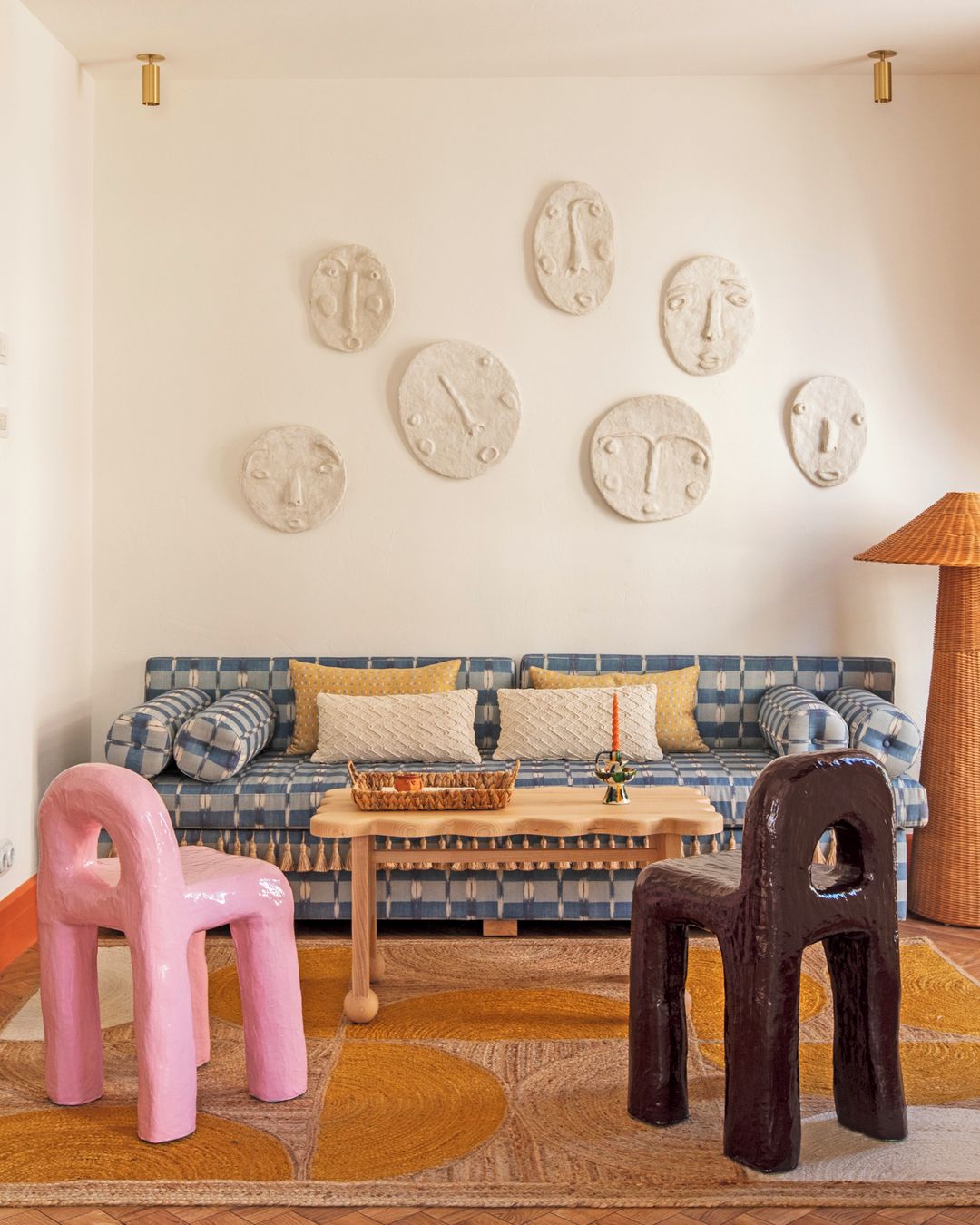 Living room featuring a blue patterned sofa, quirky chairs, a coffee table, and decorative face masks on the wall, creating a unique interior.