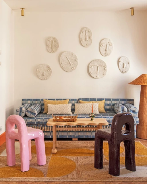 Living room featuring a blue patterned sofa, quirky chairs, a coffee table, and decorative face masks on the wall, creating a unique interior.