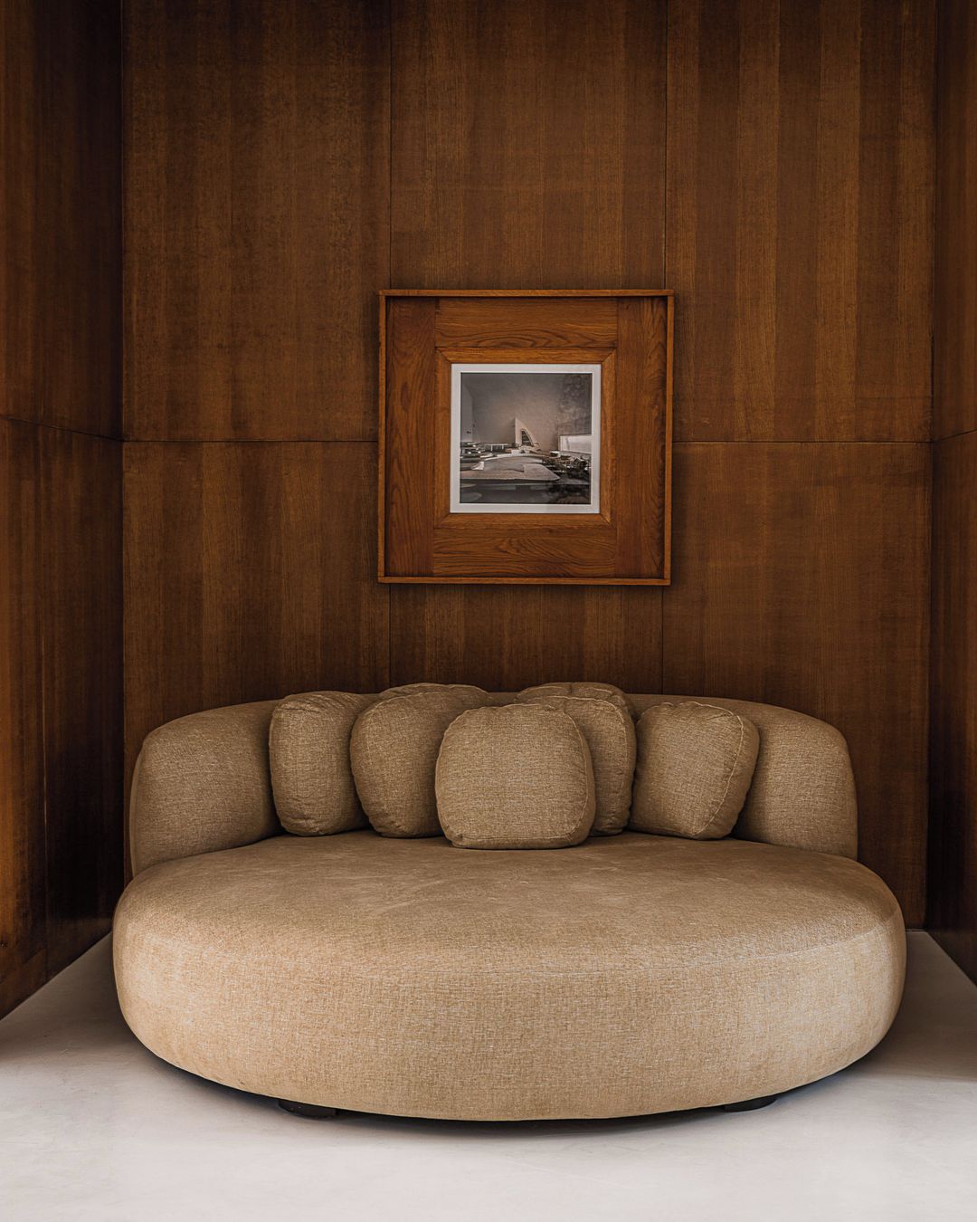 Interior design featuring a round sofa with pillows in a room with wood paneling and a framed picture on the wall.
