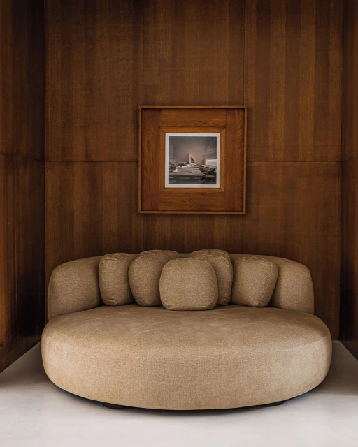 Interior design featuring a round sofa with pillows in a room with wood paneling and a framed picture on the wall.