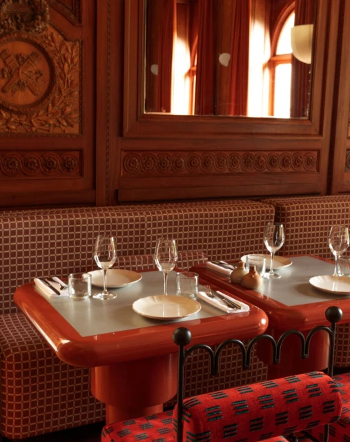 Restaurant interior with two tables set for dining, featuring plates, glasses, and silverware, in warm lighting with brown wood panelling.