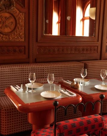 Restaurant interior with two tables set for dining, featuring plates, glasses, and silverware, in warm lighting with brown wood panelling.