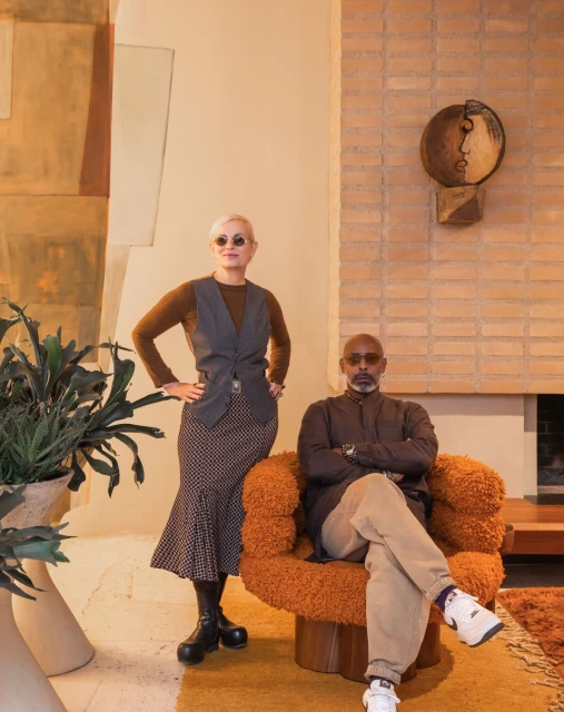 Stylish indoor portrait of a man seated in an armchair with a woman standing nearby, complemented by modern decor and neutral color tones.