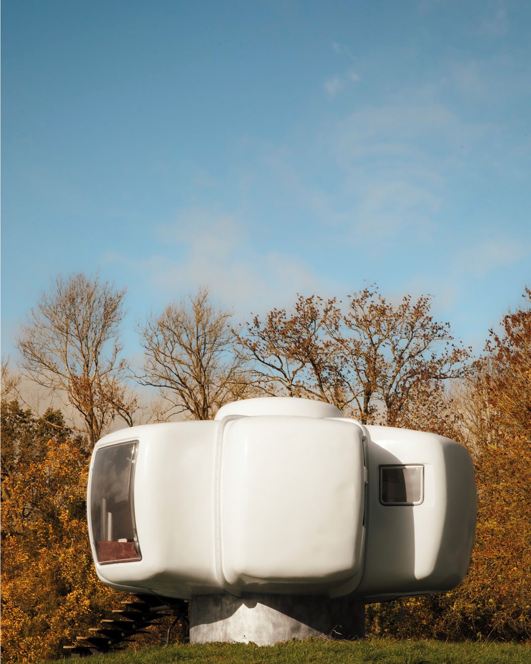 Futuristic pod house on green grass with trees in background under a clear blue sky. Unique architecture and landscape design.