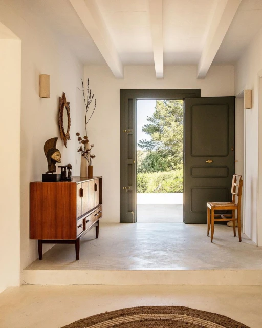 Interior view of a hallway featuring a mid-century modern cabinet, decorative mirror, and an open doorway with a view of trees.