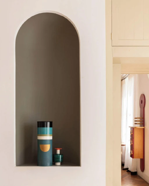 Interior shot of decorative vases displayed within a recessed arched wall niche, complemented by a cabinet with an artistic design.