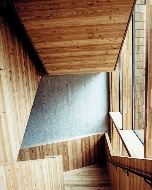 Wood-paneled interior staircase with natural light, showing steps, railing, and architectural details in a modern setting.