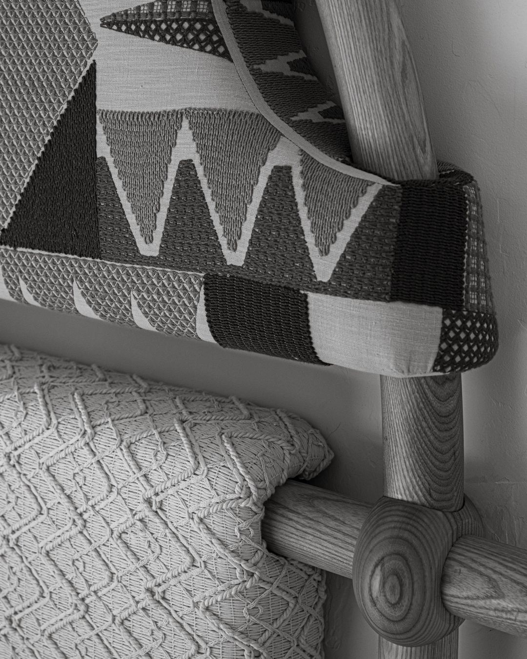 Close-up of a bed featuring a geometrically patterned headboard and a textured knit throw blanket, showcasing neutral tones and textures.