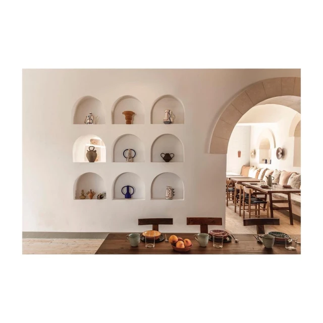 Interior design featuring a white-walled dining room with decorative pottery in arched wall niches, and set tables for dining.