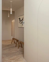 Minimalist hallway interior with neutral walls, light brick flooring, two wooden benches, and hanging pendant lights by Karel Balas