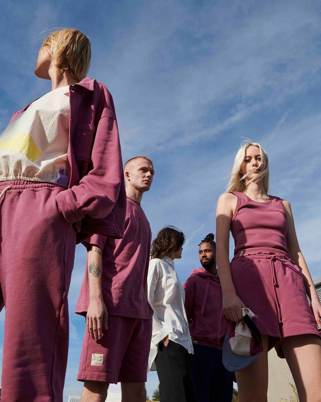 Group of five young adult fashion models wearing matching maroon sweat suits, posing in a low-angle shot against a clear blue sky.
