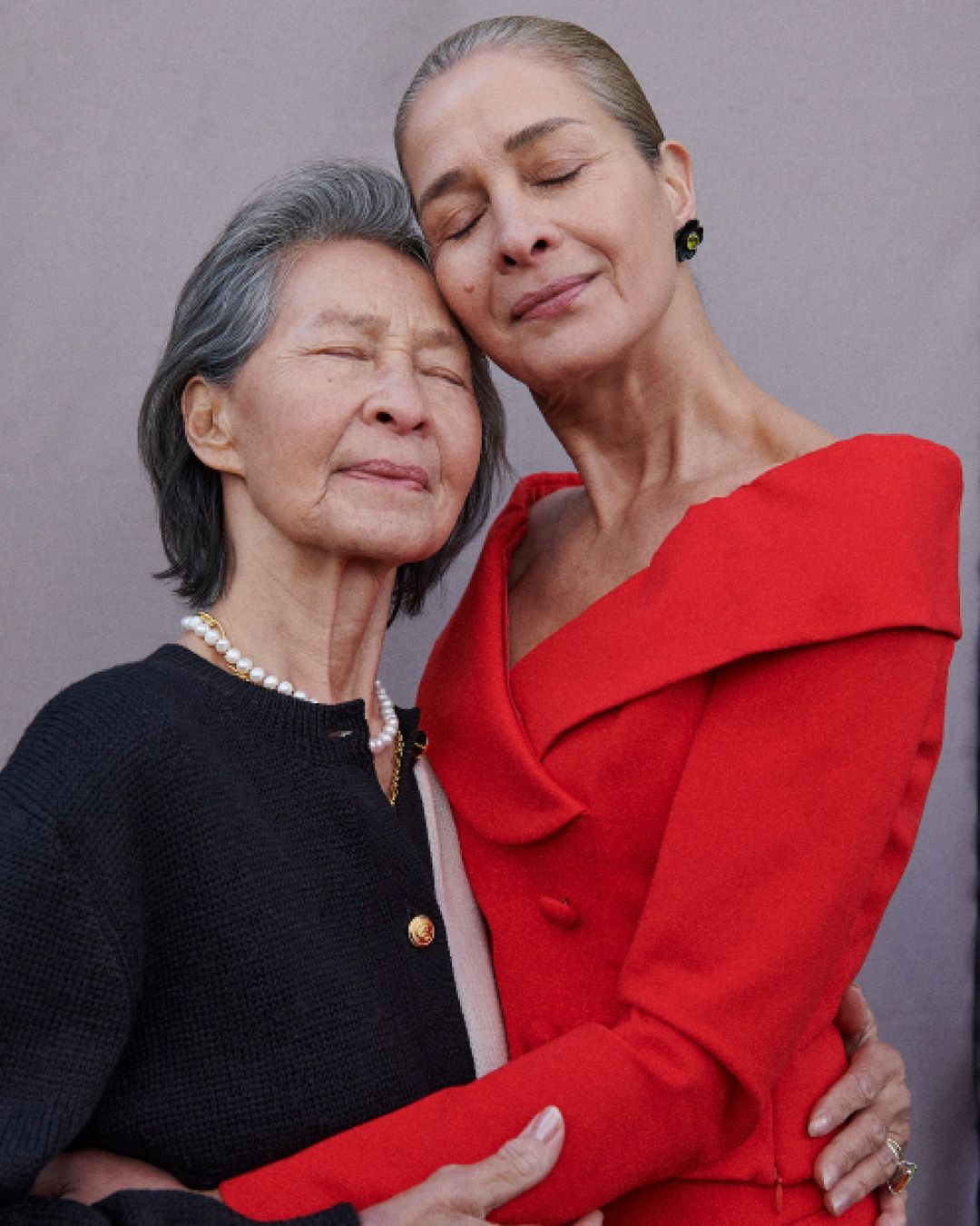 Two women embrace, one in red, one in black. Elegant, timeless style in a portrait with genuine affection and soft, natural lighting.