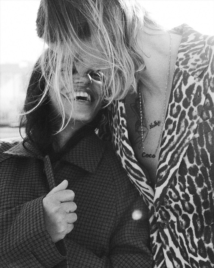 A joyful couple laughs together; the blonde-haired man wears a leopard-print jacket, while the brunette woman wears a patterned coat.