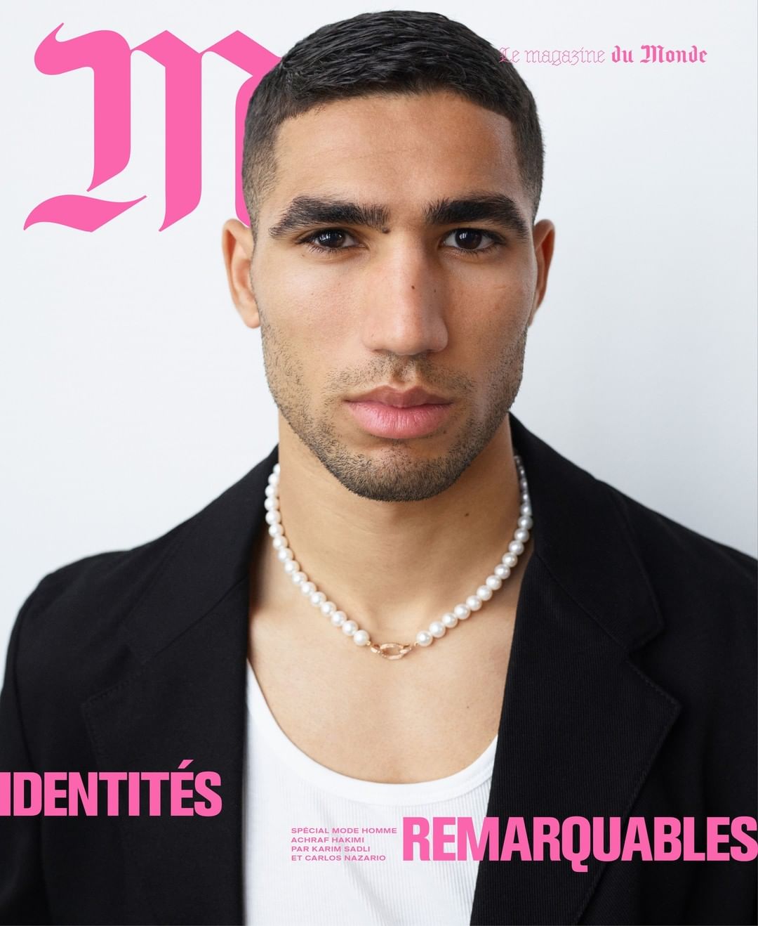 Portrait of Achraf Hakimi wearing a white tank top, black blazer, and pearl necklace against a plain white background