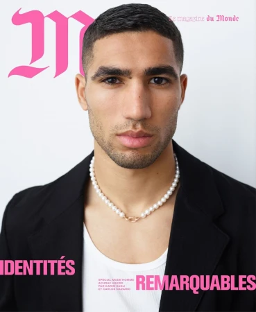Portrait of Achraf Hakimi wearing a white tank top, black blazer, and pearl necklace against a plain white background