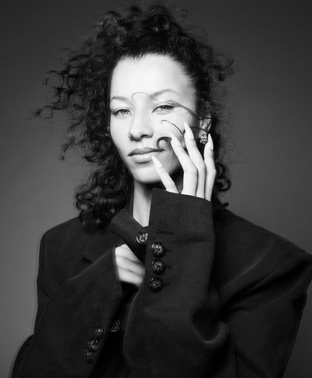 Black and white portrait of a woman with curly hair wearing a dark blazer, photographed by Karim Sadli.