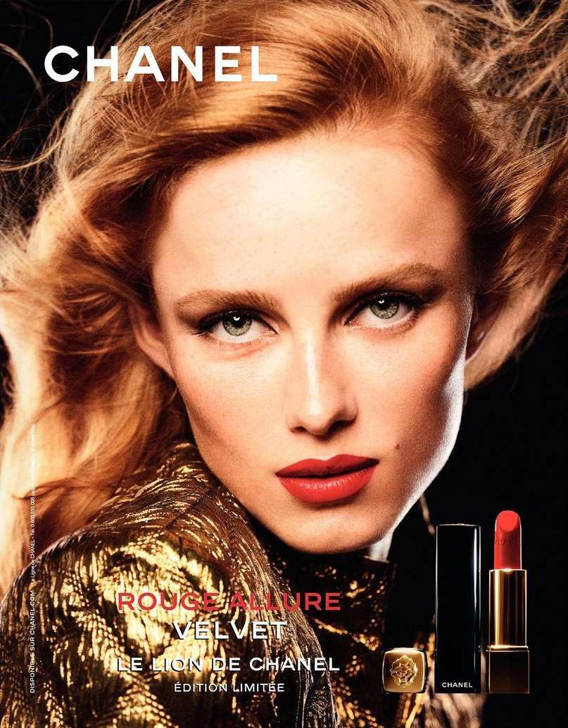 A striking beauty advertisement featuring a red-haired woman in a gold jacket with red lipstick, alongside Chanel's Rouge Allure Velvet lipstick.
