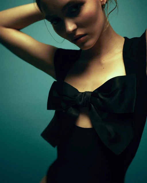 Woman in a black bodysuit with a large bow poses in front of a turquoise background. Fashion portrait featuring elegant design.