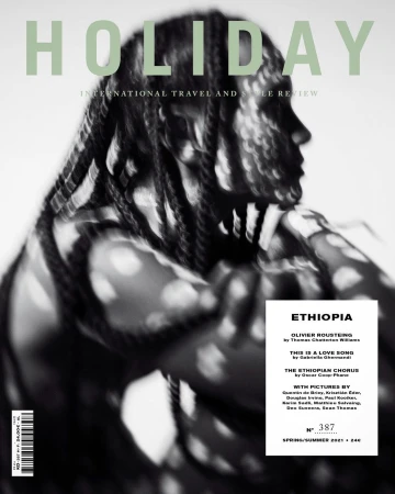 Holiday magazine cover featuring a Black model with braided hair and an abstract background. The focus is on travel and style.