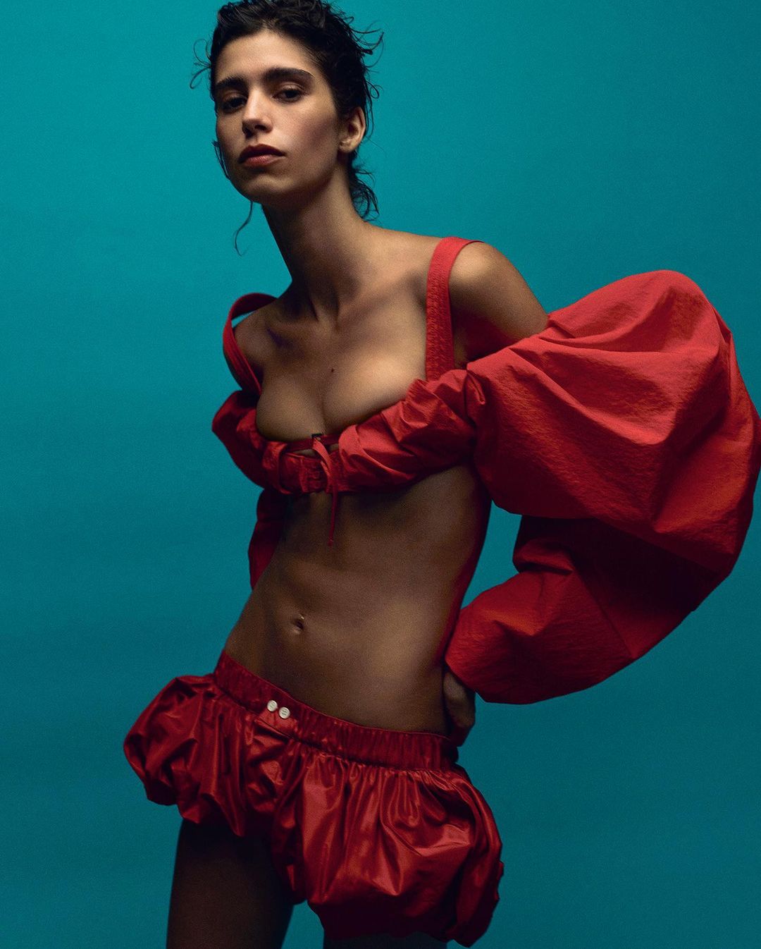 Model in voluminous red off-shoulder top and matching shorts against a solid blue background by Karim Sadli.