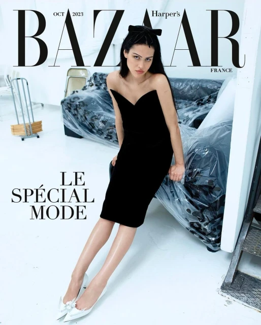 Fashion magazine cover featuring a woman in a black dress and bow, sitting in a studio with Bazaar and Harper's Bazaar text.