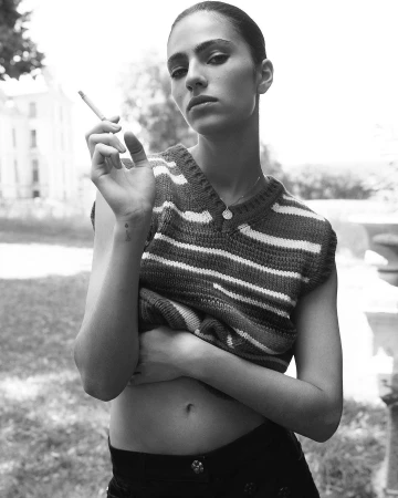 Monochrome portrait of a woman in a striped sweater holding a lit cigarette outdoors, captured by Karim Sadli.
