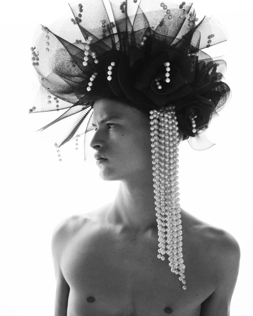 Portrait of a topless person wearing a dramatic black floral and pearl headpiece against a stark white background in black and white.