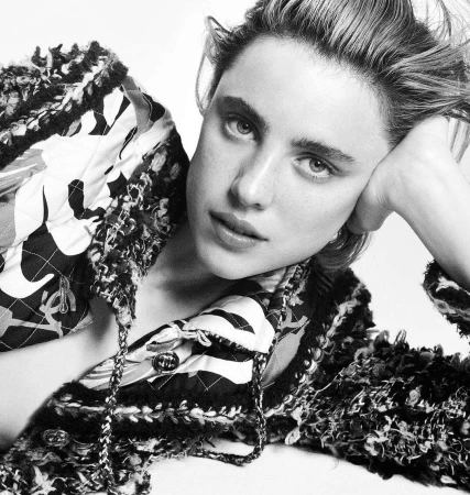 Close-up portrait of a woman resting head on hand wearing a textured patterned jacket against a plain background