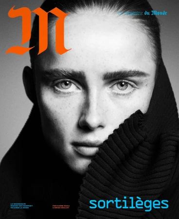 Close-up magazine cover portrait of a woman with dark hair, wearing a black turtleneck, contrasted against a neutral gray backdrop.