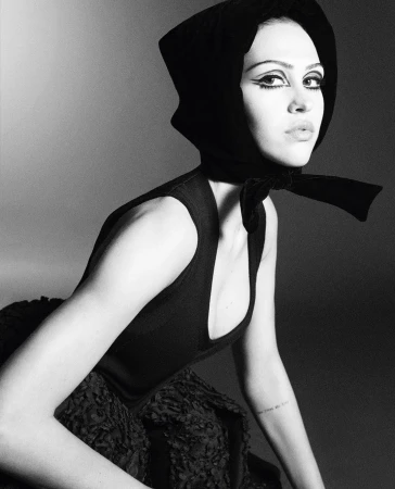 Monochrome portrait of a woman with dramatic eye makeup wearing a black headscarf and a sleeveless top, gazing towards the camera.