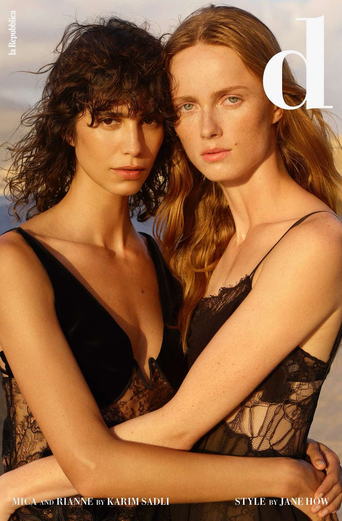 Two women embrace in lace dresses. A fashion editorial showcases two adult models against a soft neutral background in medium shot.