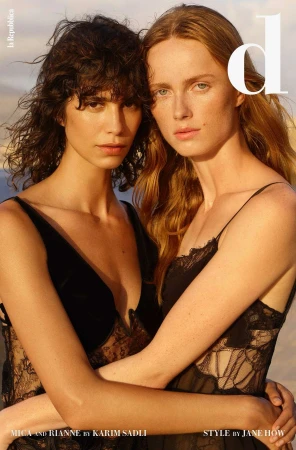 Two women embrace in lace dresses. A fashion editorial showcases two adult models against a soft neutral background in medium shot.