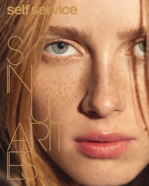 Close-up portrait of a fair-skinned woman with freckles, light red hair, and light blue eyes, featuring the 'Self Service' magazine logo.