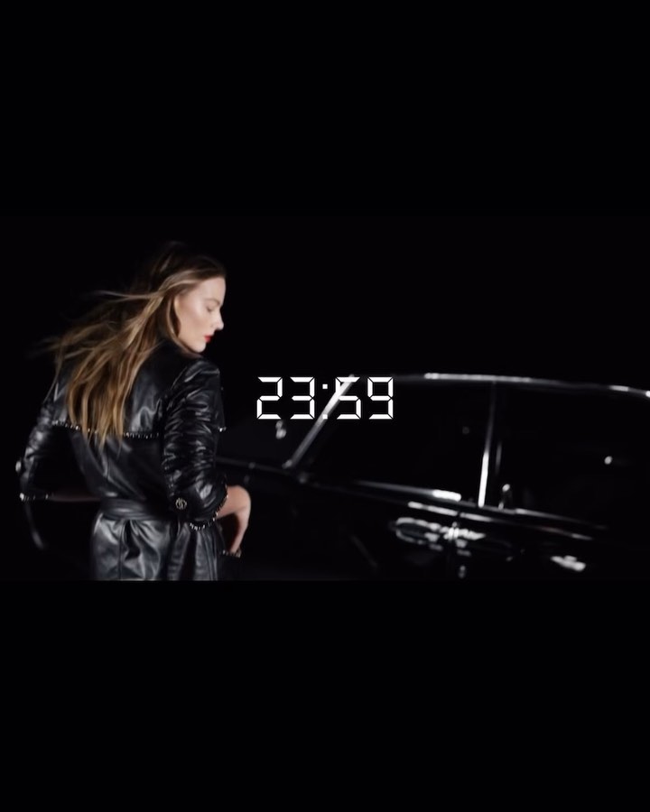 Stylish woman in a black leather trench coat near a limousine at night, creating a dramatic and fashionable street scene.