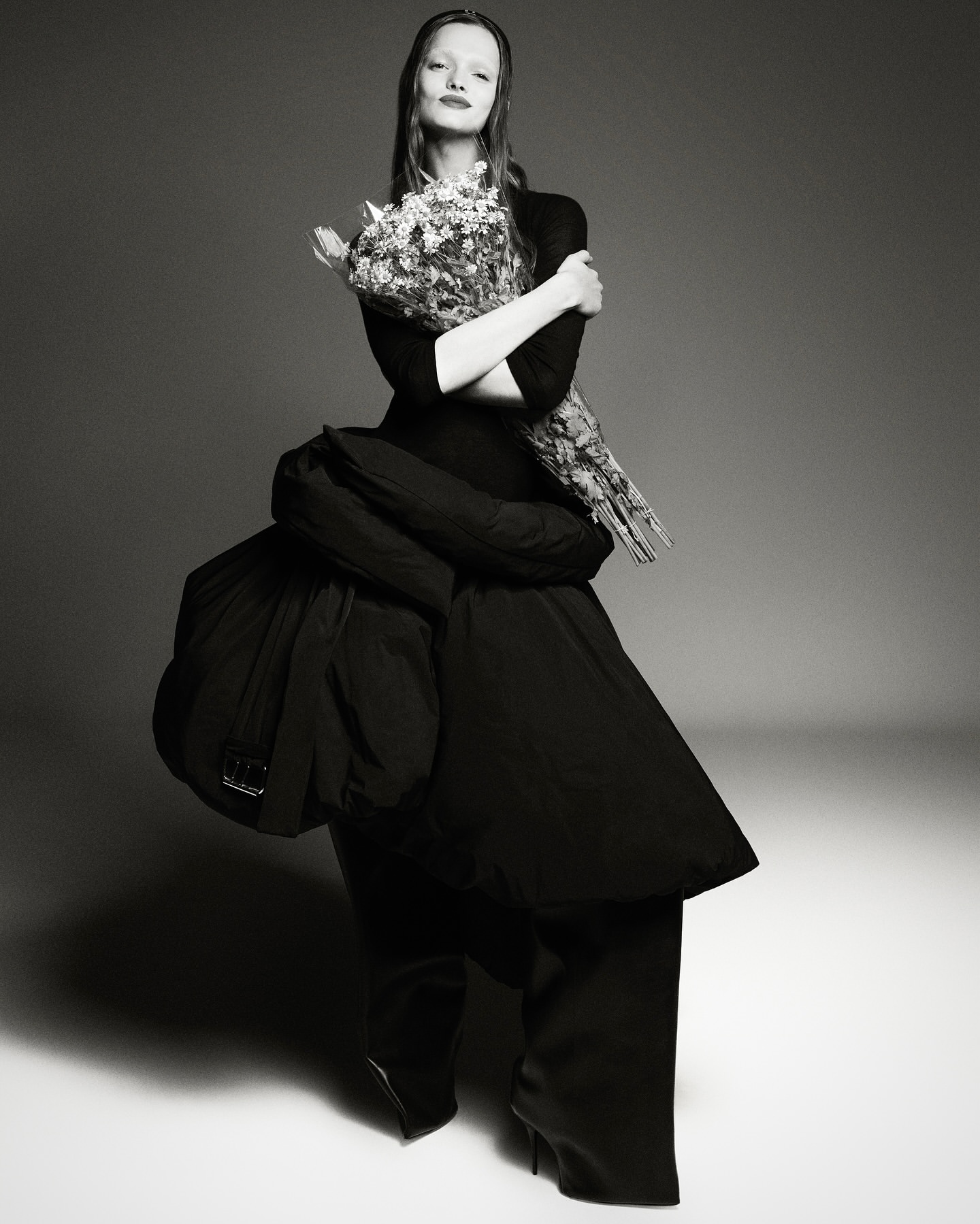 Black and white studio portrait of a woman in a puffy black dress holding flowers, showcasing high fashion in a studio setting.