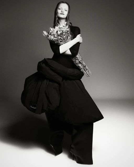 Black and white studio portrait of a woman in a puffy black dress holding flowers, showcasing high fashion in a studio setting.