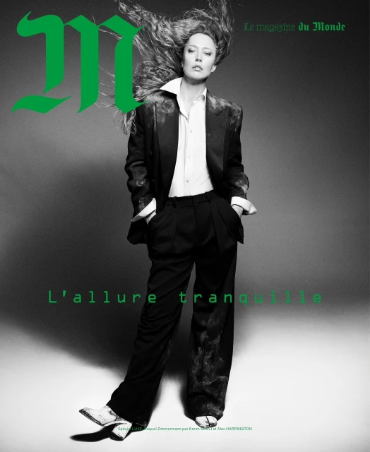 Magazine cover featuring woman in oversized black suit and white shirt, with loose wavy hair, against a grey backdrop. 