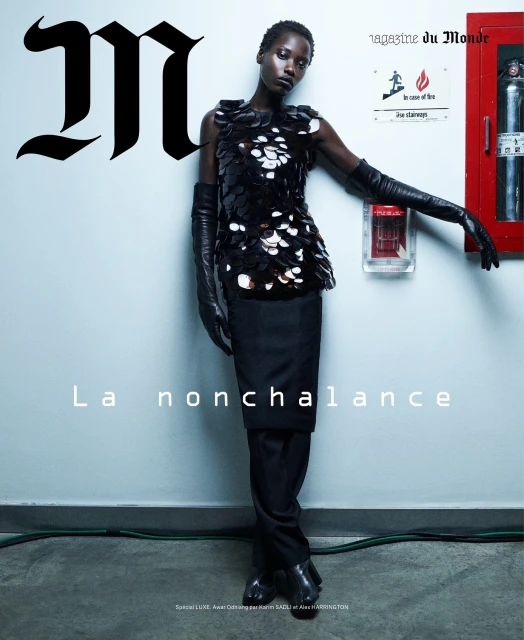 Magazine cover featuring a Black woman in a sequin top, long gloves, and dark trousers posing against a pale blue-grey wall with fire safety equipment.