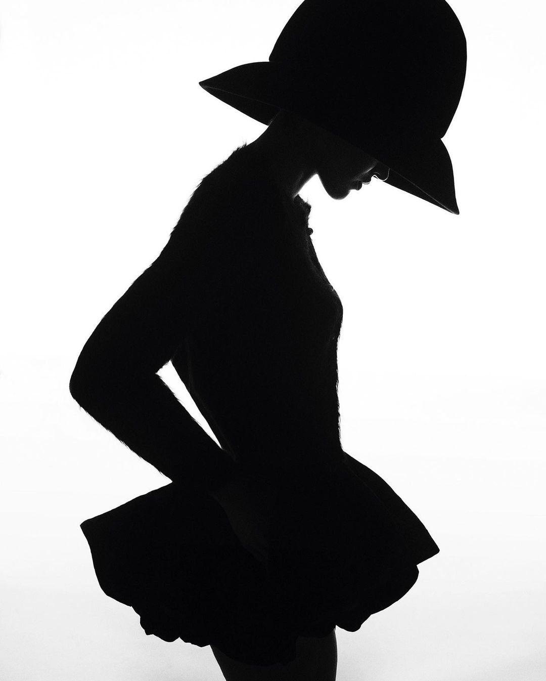 Silhouette of a woman wearing a wide-brimmed hat against a bright white background