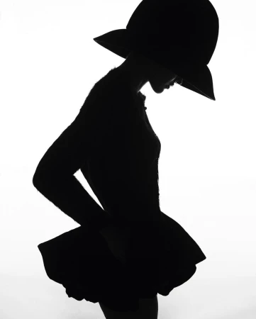 Silhouette of a woman wearing a wide-brimmed hat against a bright white background