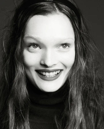 Close-up portrait in black and white of a smiling adult woman with long hair and a headband, wearing a dark turtleneck sweater.