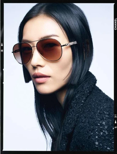 Close-up of an adult woman wearing aviator sunglasses with black frame, wearing a black coat and sporting short, dark hair, and light skin.